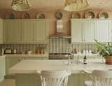 The kitchen area is demarcated by a vast island and bespoke cabinetry painted sage green.