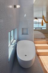 Hanna’s sleeping suite includes a bathtub by Badeloft. Windows, cut into walls covered with matte white porcelain penny tiles with blue grout, provide views. Only the home’s concrete raft “basement” is windowless; it contains a Tesla battery, the water pump, and storage closets.  Photo 10 of 12 in Bathrooms by Inès Le Cannellier from An Unorthodox Houseboat in Sausalito Gives Its Owner Permission to Play