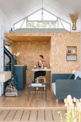 The kitchen includes a range and a hidden pull-out table nestled between cabinets. The living room area includes a brass and leather firewood tray from Ferm Living and ceramic pieces made by Eugenia, including coffee mugs and an incense holder.