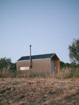 The cabin is clad with corrugated metal panels. The rectangular window is positioned over the kitchen to let in light and air.  Photo 4 of 13 in My House: A Roaming Couple Settle Down by DIYing a Tiny Cabin for Less Than $10K from The 10 Teeniest Tiny Homes of 2023