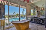 In the en suite bathroom, a soaking tub overlooks the home’s pool and the desert landscape beyond.