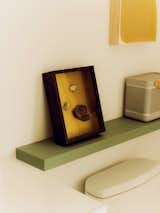 Framed stones and portable Bluetooth speaker on green shelf above toilet. 