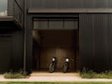 Two motorcycles parked within a workshop in a black-stained wood-clad home.
