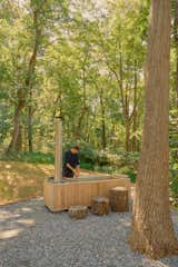 Man cleaning a wood-fired hot tub in a forest.