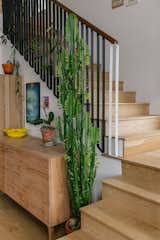 Landing of light hardwood stairs beside cabinet, potted plants, and vines that wrap around black metal balusters.  