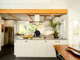Man works in sunny, U-shaped kitchen with exposed wood beams.