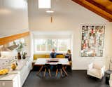 View from upstairs landing of couple sitting on bench in dining room beneath double-height ceiling with exposed wood beams.