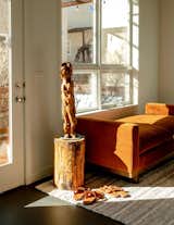 Wood statue stands on a pedestal by velvet chaise lounge in entryway.