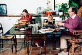 A photo from a 1972 photoshoot for Vogue magazine by fashion photographer Henry Clarke. At the dining room table with writer Joan Didion, novelist John Gregory Dunne, and their adopted daughter, Quintana Roo, in their Malibu, California home. Didion and Quintana Roo are seated on Hitchcock chairs, while Mr. Dunne sits in a peacock wicker chair as they eat at the Federal era drop leaf table. The floor is terracotta Mexican tile. (Henry Clarke/Condé Nast/Shutterstock)   Photo 1 of 101 in NB by Jane Dailey from The Photos of Joan Didion That Defined the Californian Kitchen