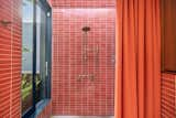 One of the bathrooms comes with a large shower wrapped in red subway tile.