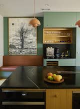 Beside the coffee bar in the kitchen, a work by Mike Saijo is displayed above a custom leather-upholstered banquette. The team chose soapstone for the island and the counter.