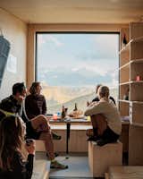 The author and BCW architect Skye Sturm, with Skye’s husband and two local hikers, sit at the picture window at the front of Bivacco Brédy. Skye and architects Facundo Arboit and Chiara Tessarollo designed the bivacco. Located next to the Laghi di Dziule, it sleeps six in about 130 square feet and has a solar panel to recharge mobile phones.&nbsp;&nbsp;