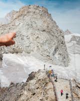 A tourist points toward Mont Blanc as others hike on a glacier covering its surface.&nbsp;