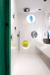 Bathroom with green door, open rain shower, round windows with wall cleats, white walls and floors, and Rocca faucets