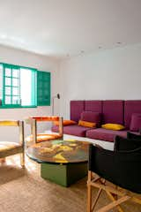 Living room with green window, beige rug, chairs, coffee table with abstract art, and red-violet sofa bench