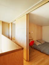 View of bedroom with small desk, red chair, low bed, and sliding wood door from stair landing