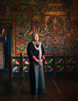 Bhutanese author Kunzang Choden stands in room with dark wood floors, walls with orange and green murals in Ogyen Choling, a fortress-village  in Bhutan