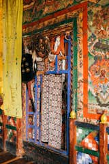 Traditional mask hand on wood lattice in nook in walls with colorful murals in Ogyen Choling, a fortress-village in Bhutan
