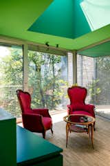 Room with green storage and ceiling, skylight, floor-to-ceiling glass windows and doors, and red velvet armchairs around round wood coffee table in Turin, Italy