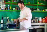 Man fries food on electric range in kitchen with green shelving and walls in Turin, Italy