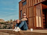 Man sits on porch with white mug outside wooden tiny home in Sintra, Portugal
