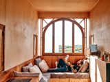 Man lays in nook beneath arching wood-framed window reading a book in wooden tiny home in Sintra, Portugal