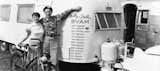 Black-and-white photograph of Wally and Stella Byam posing outside their Airstream with list of places across the world to which they travelled in it painted on the side