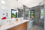 In addition to offering direct outdoor access, the primary suite has a large glass shower, a soaking tub, and a double vanity.