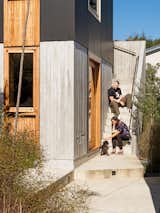 Kris and Jess Sowersby, owners of Klim Type Foundry, sit on the exterior concrete staircase up to the second story of their additional dwelling unit in Miramar, Wellington, New Zealand with black aluminum, board-formed concrete, and medium-stained wood siding.