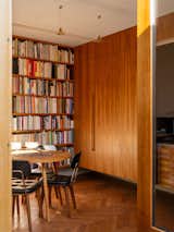 Home office with oak parquet flooring, built-in shelving, rimu wood cabinetry, wood chairs with black leather upholstery and long brass overhead pendant lamp in additional dwelling unit in Miramar, Wellington, New Zealand.