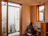 Jess Sowersby, co-owner of Klim Type Foundry, works beside open glass door framed in medium-stained wood that leads out onto concrete walkway lined with shrubs and tree in home office with rimu wood cabinetry and Brazilian quartzite tables in additional dwelling unit in Miramar, Wellington, New Zealand.