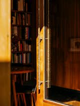 Detail of sculptural brass handle of glass door framed in medium-stained wood on ground story of additional dwelling unit in Miramar, Wellington, New Zealand.