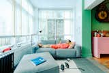 Jonathan Solomon lounges on grey couch in reading room with slate tile floors, white-painted brick walls, large windows, black radiator, black floor lamp, and thick white rug in postmodern pomo renovation of 19th century Uptown Chicago home.