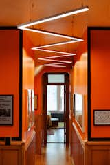 The tight, orange hallway upstairs is packed with art, including Meg’s grandmother’s drawings of the Chicago skyline. A zigzagging light that Meg assembled with components from a commercial office supply company leads the way to the primary bedroom and library.