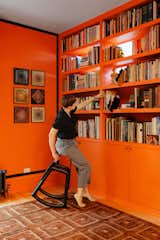 The house’s “cavalier” approach to windows is Dunn’s favorite part of the project—there are bookshelves in front of them in the library. “It’s a fun way of dignifying what has come before but also not being overly deferential to it,” Dunn says. The room is painted in Sherwin-Williams’s Obstinate Orange, and Meg sits on a seating prototype by Norman Teague.