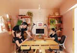 Jag Studio—Juan Alberto Andrade, Cuqui Rodríguez, their daughter, and their colleague Victoria Peralta—work at light wood table in their office in Guayaquil, Ecuador with pink walls and ceiling, light wood flooring, pink metal cabinets, desk lamps, apple computers, and potted plants.