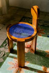 Chuch Estudio chair in medium toned wood with cobalt blue seat stands on floral green and orange tiles.