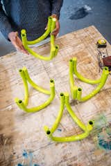 Andu Masebo handle metallic objects made of three curving yellow-green tubes that form furniture legs or feet.