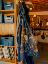 Paint-stained denim apron hangs from book on wood millwork shelving unit in Los Angeles workshop of Adi Goodrich, founder of Sing Thing.