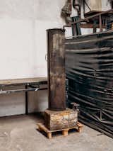 Rusted metallic column stands on brick and wood plinth in Tejumola Butler Adenuga’s London studio workshop.