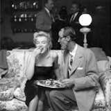 marilyn laughing and eating in a black dress on a floral couch next to a photographer