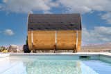 Redwood Outdoors barrel panorama sauna with asphalt shingle roof sits beside pool with concrete deck in desert landscape.