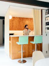 Man draws open original yellow acrylic screens separating living room from kitchen bar with wood cabinetry  and Corian countertops in Los Angeles Hamilton House, designed by postwar architect Kazuo Umemoto, modernist midcentury home renovated by Sonya Lee.