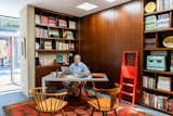 Man sits at metal desk in wood-paneled study library with red and brown geometric rug with slate floor in midcentury internationalist home in Wyomissing, Pennsylvania by Muhlenberg Brothers and renovated by Kevin Yoder and Louise Cohen.