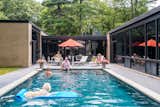 People swim in lounge beside large pool outside brick and glass facade of midcentury internationalist home in Wyomissing, Pennsylvania by Muhlenberg Brothers and renovated by Kevin Yoder and Louise Cohen.