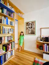 Girl stands in archway beneath wood millwork library bookcase shelves with blue laminate surfaces in Brooklyn apartment renovated by Spot Lab.