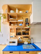 Millwork plywood storage housing tableware above blue countertop in kitchen with wood cabinetry in Brooklyn apartment renovated by Spot Lab.