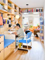 Man works at plywood desk beneath wood millwork library shelves bookcase in Brooklyn apartment renovated by Spot Lab.