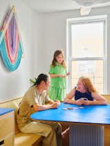 Man, woman, and daughter family play cards at blue dining table in long curving wraparound bench in breakfast nook in Brooklyn apartment renovated by Spot Lab.