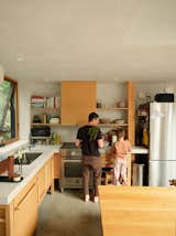 Father and child work in kitchen with concrete floors, wood cabinetry, and marble countertops in home by Andrew Frederick in Owls Head, Maine.